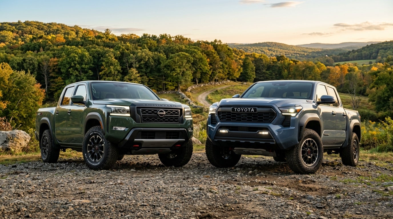 A green Nissan Frontier and a blue Toyota Tacoma parked side-by-side on a gravel road with hills in the background.