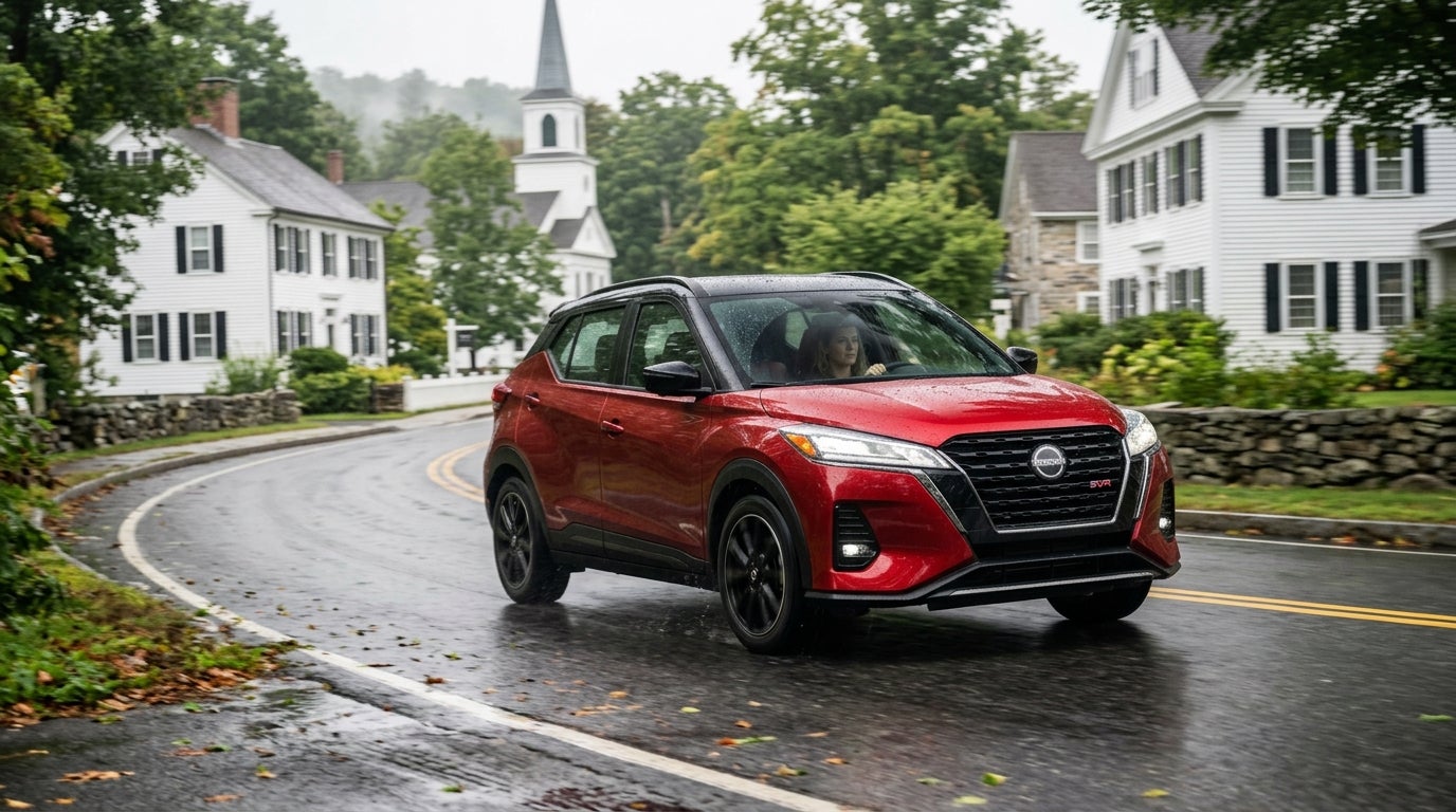 Red Nissan SUV driving on a wet, winding road through a historic New England village on an overcast day. (Representative image for illustration purposes only. Actual vehicle may vary based on trim and configuration.)