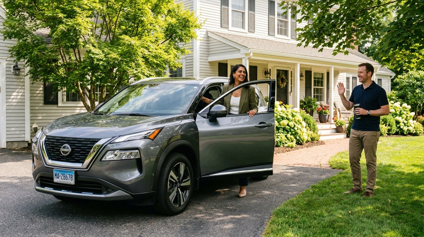 A woman stepping out of a grey Nissan SUV in a driveway, smiling at a man waving from the lawn of a suburban house. (Representative image for illustration purposes only. Actual vehicle may vary based on trim and configuration.)