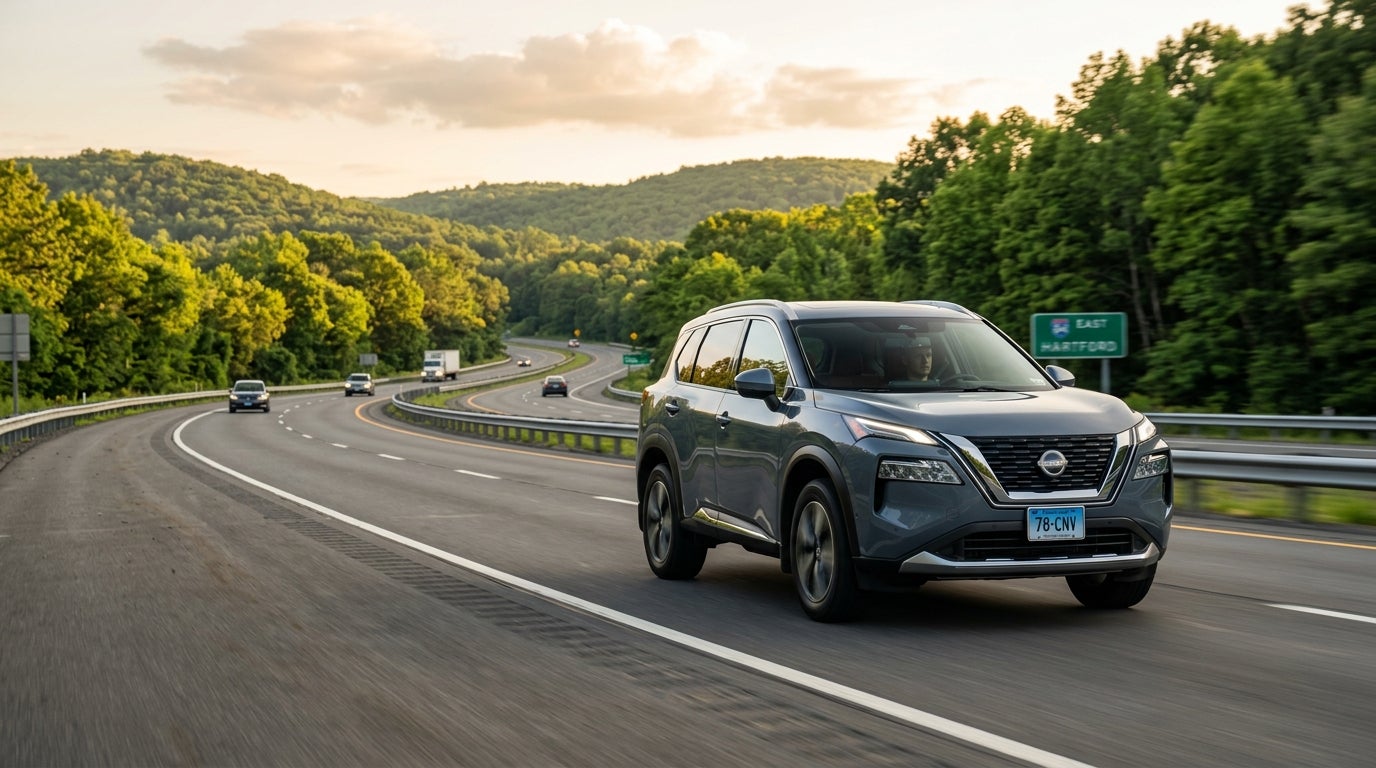 A grey Nissan Rogue SUV driving along a winding highway surrounded by green forest during golden hour. (Representative image for illustration purposes only. Actual vehicle may vary based on trim and configuration.)