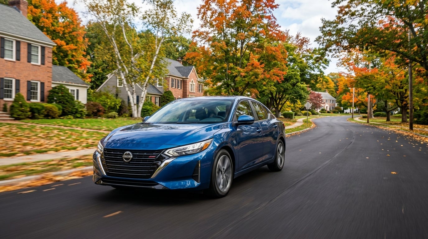 A blue Nissan sedan drives down a tree-lined residential street filled with colorful autumn foliage. (Representative image for illustration purposes only. Actual vehicle may vary based on trim and configuration.)