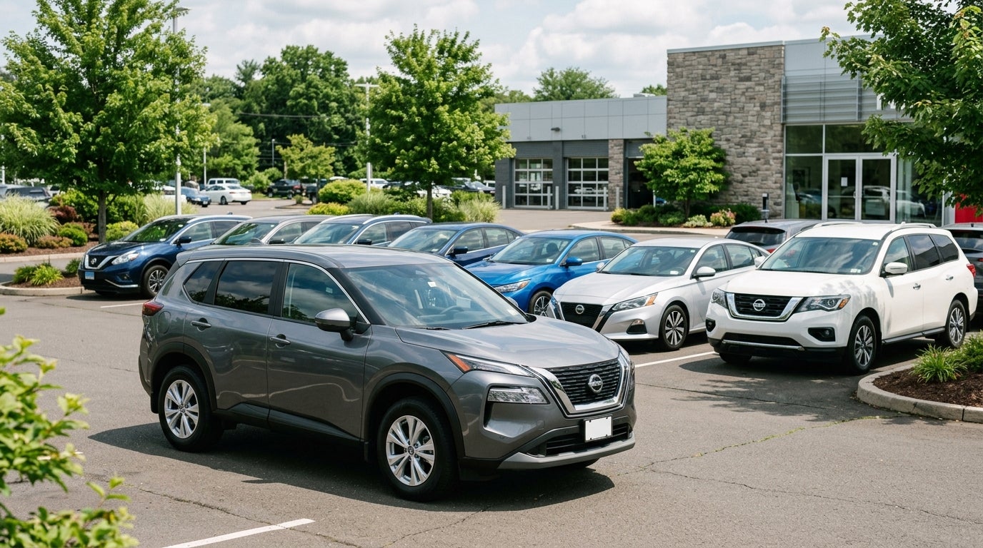 A grey Nissan SUV parked in front of other Nissan sedans and SUVs at a car dealership lot. (Representative image for illustration purposes only. Actual vehicle may vary based on trim and configuration.)