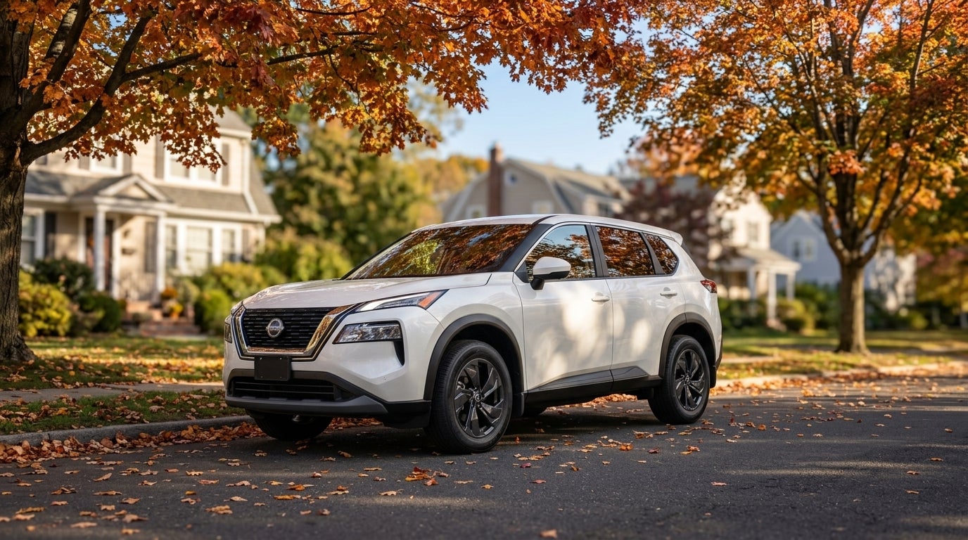 White Nissan Rogue SUV parked on a residential street surrounded by vibrant orange autumn foliage and leaves. (Representative image for illustration purposes only. Actual vehicle may vary based on trim and configuration.)