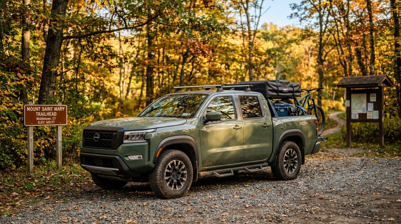 Olive green Nissan Frontier truck equipped with camping gear parked at a trailhead during autumn. (Representative image for illustration purposes only. Actual vehicle may vary based on trim and configuration.)