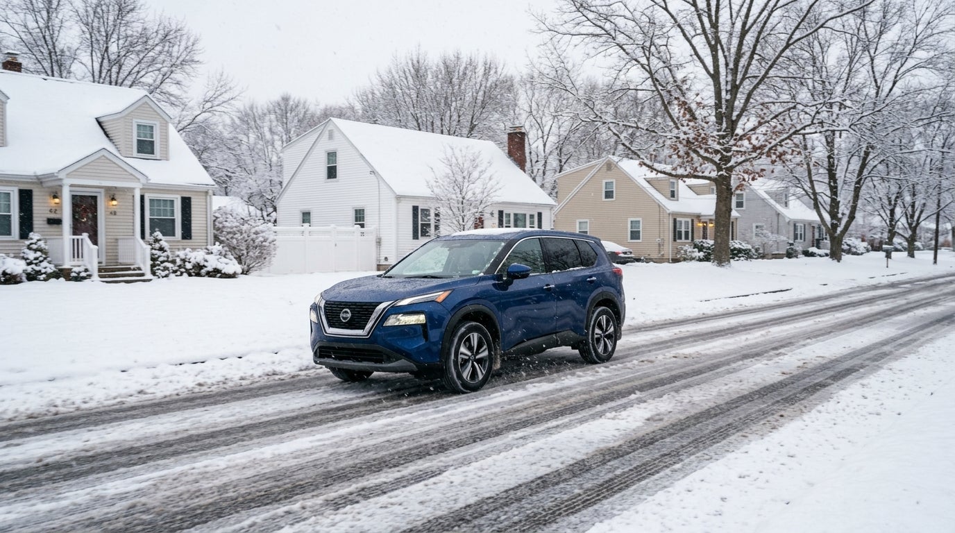Blue Nissan Rogue SUV driving on a slushy, snow-covered suburban road past winter houses. (Representative image for illustration purposes only. Actual vehicle may vary based on trim and configuration.)