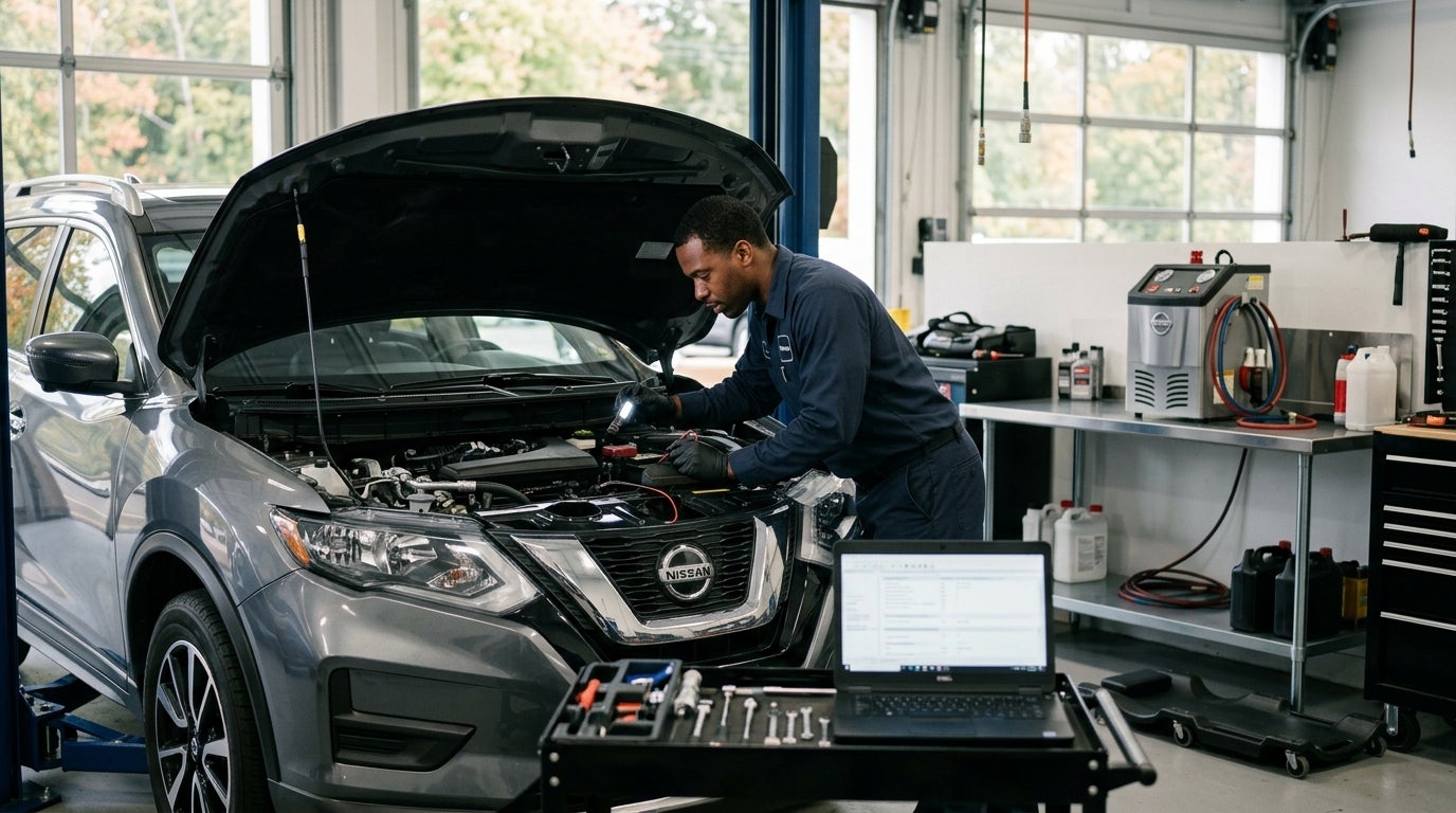Mechanic using diagnostic tools under the open hood of a grey Nissan SUV in an auto repair shop. (Representative image for illustration purposes only. Actual vehicle may vary based on trim and configuration.)